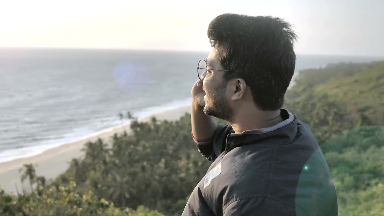 joven viajero o turista con chaqueta y gafas sentado en la cima de una montaña