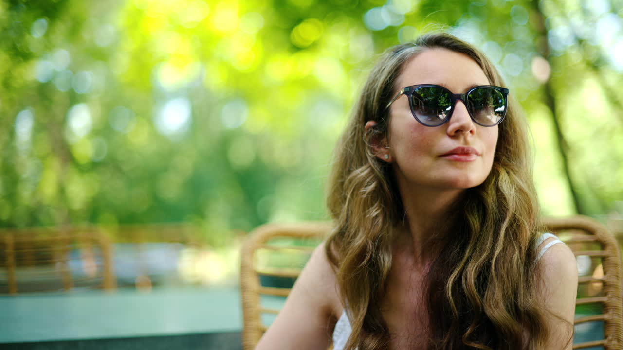 Woman wearing sunglasses looking around at a table surrounded by trees