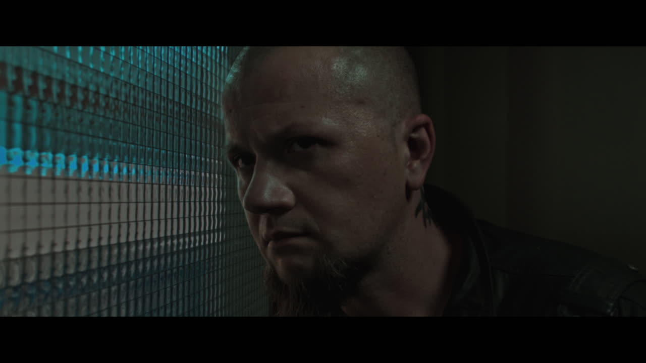 A bald dangerous looking man checks the corridor through reinforced glass