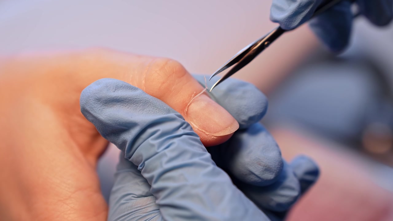 Foto macro em salão de uma manicure removendo o excesso da cutícula com tesoura fina, destacando a preparação precisa para manicure a seco, a higiene e o detalhamento profissional cuidadoso das unhas.