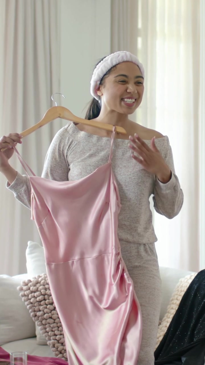 Vertical video: Hearing voice, woman in gray set at home holding pink dress on hanger laughing