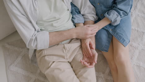vista superior de una pareja irreconocible tomándose de la mano y abrazándose mientras se sientan juntos en una alfombra en casa