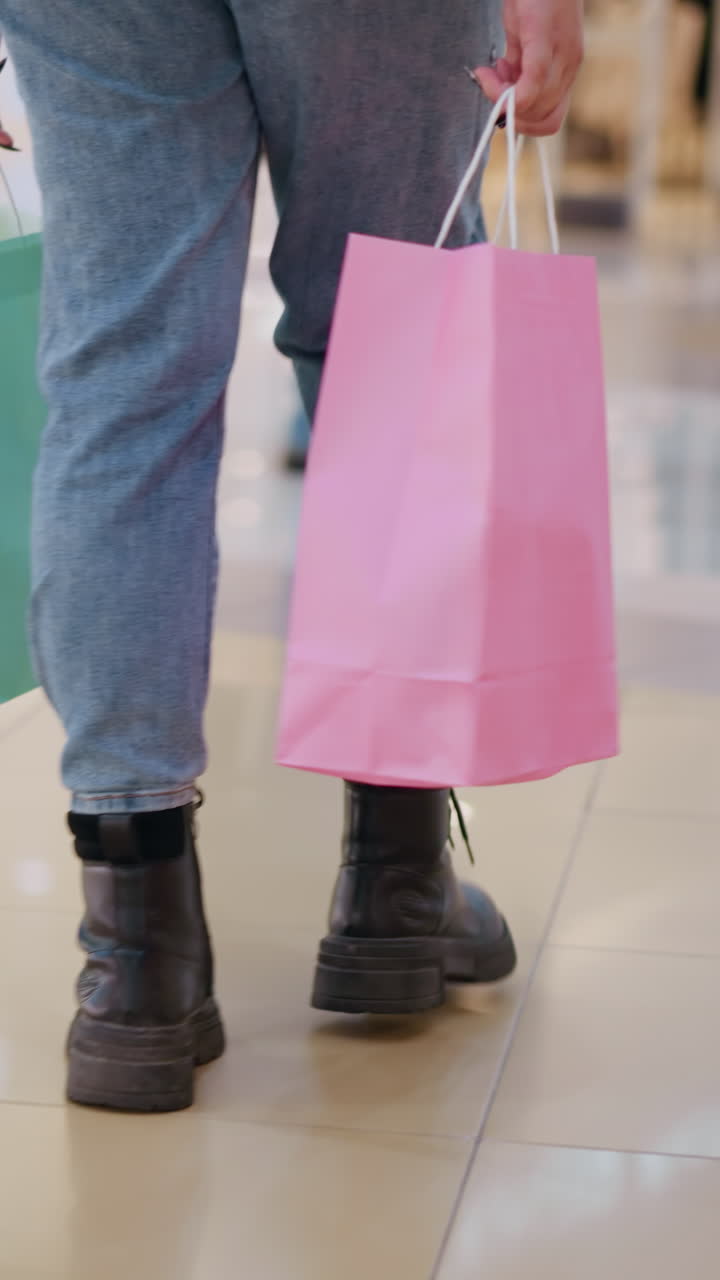 바쁜 소매 환경에서 지나가는 다른 쇼핑객들의 흐릿한 배경으로 쇼핑 가방을 들고 쇼핑몰에서 는 여성의 뒷면