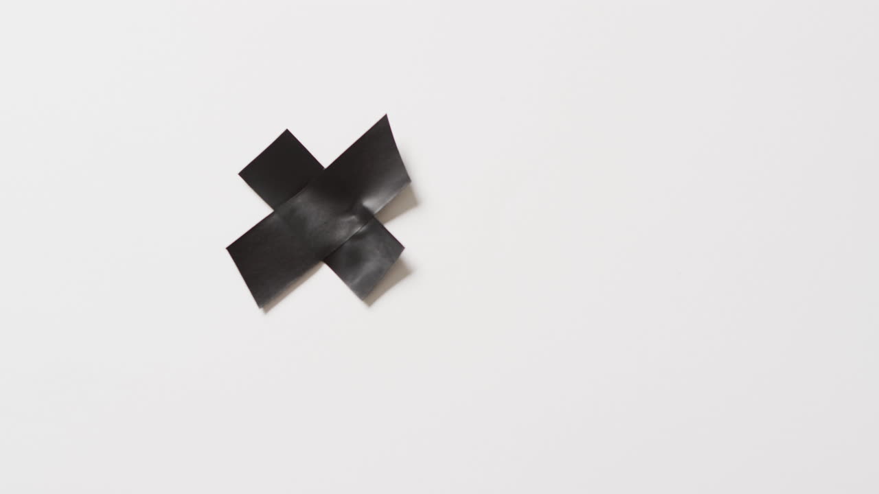 Video of close up of black tape forming cross on white background