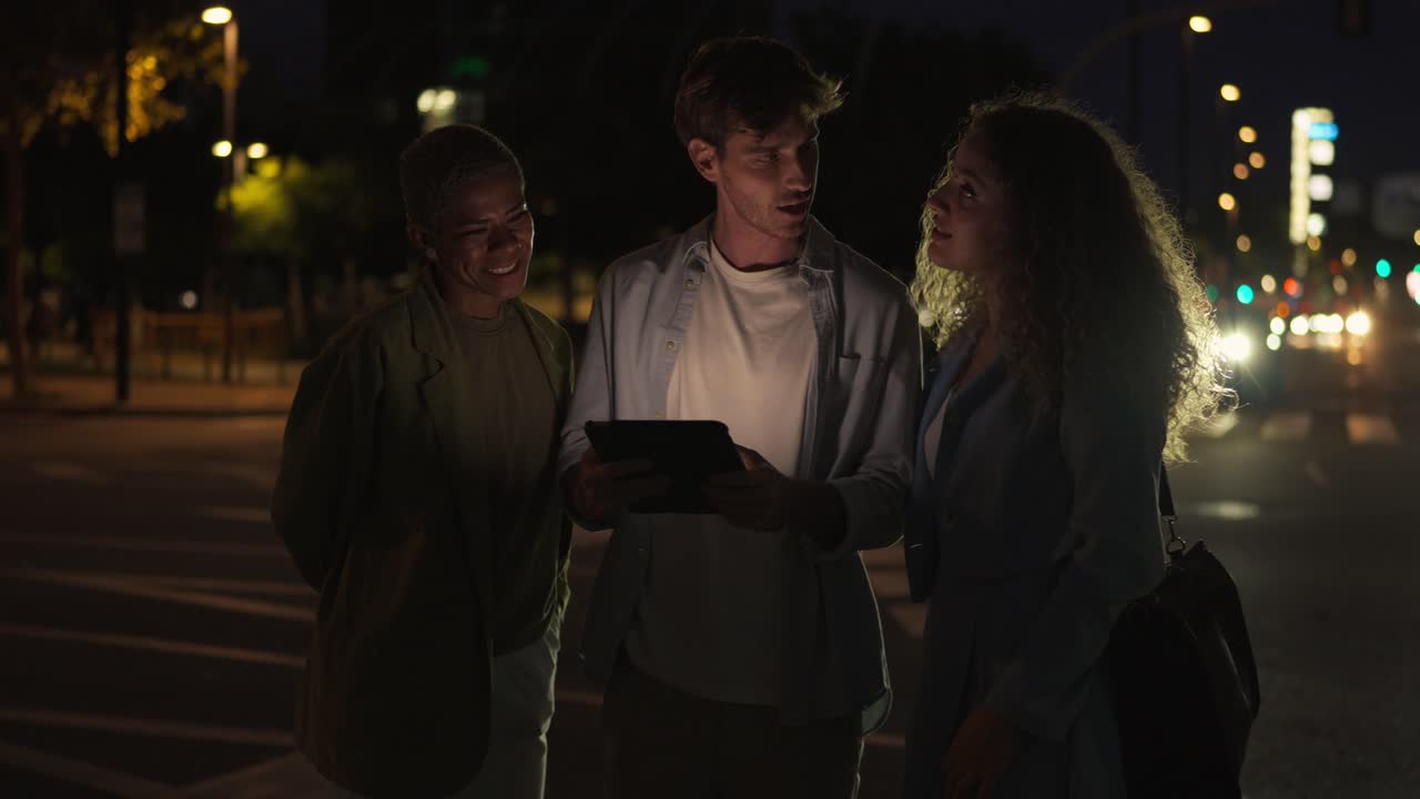 Three people talking while using a tablet at night
