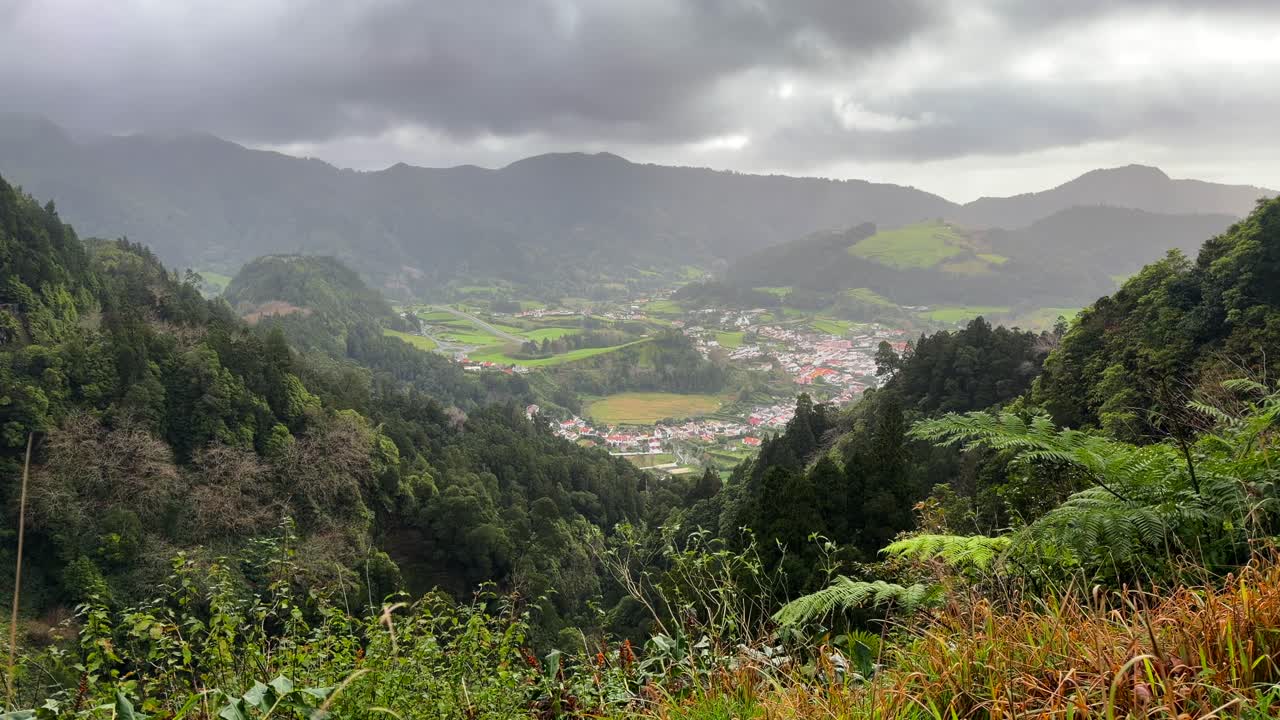 Vale de montanha verde com edifícios de aldeia em São Miguel, Açores, Portugal.