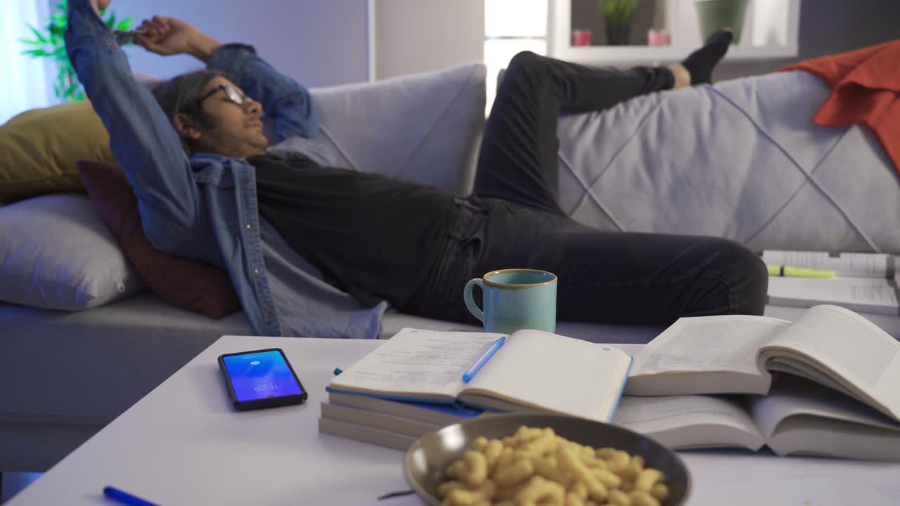 Tired lazy man lying on the sofa being woken up by the alarm clock.