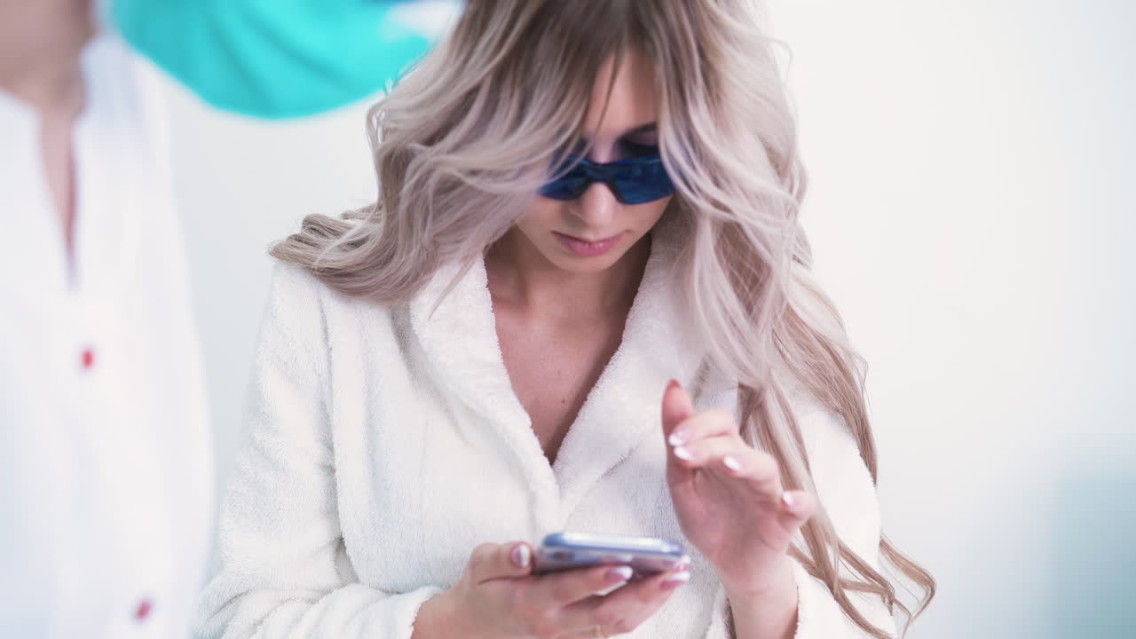 una donna con uno smartphone si sottopone a una procedura di epilazione laser