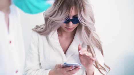 mujer con teléfono inteligente se somete a un procedimiento de depilación con láser