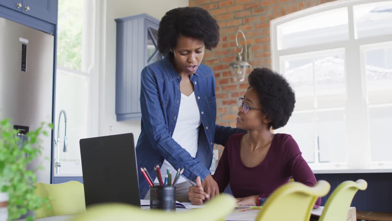 Madre e figlia afroamericane felici che fanno i compiti insieme in cucina.