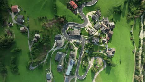 overhead aerial tilt-down view captures cars navigating a winding road in the quaint village of la val, south tyrol, italy. lush green hills flank the picturesque scene. camera moves up. lupa creative