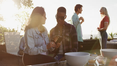 Two-friends-drinking-discussing-and-using-a-smartphone-on-a-rooftop