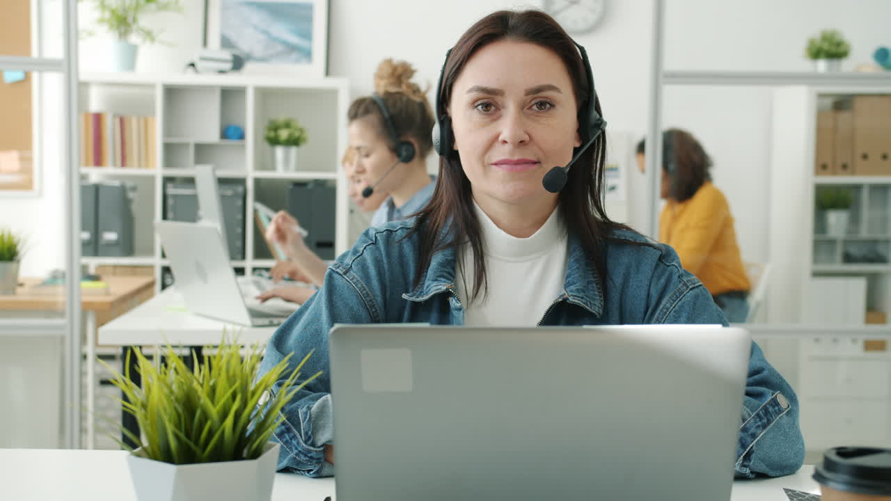 Woman in headset using laptop in a busy office
