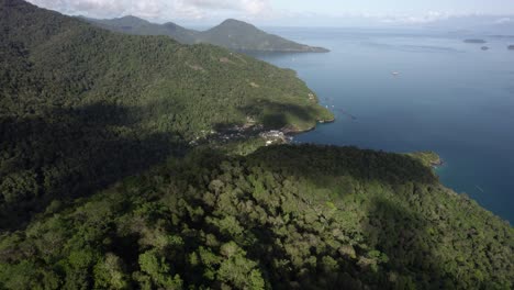 elevated aerial view diving down from the mountains towards a town on ilha grande, sunny brazil