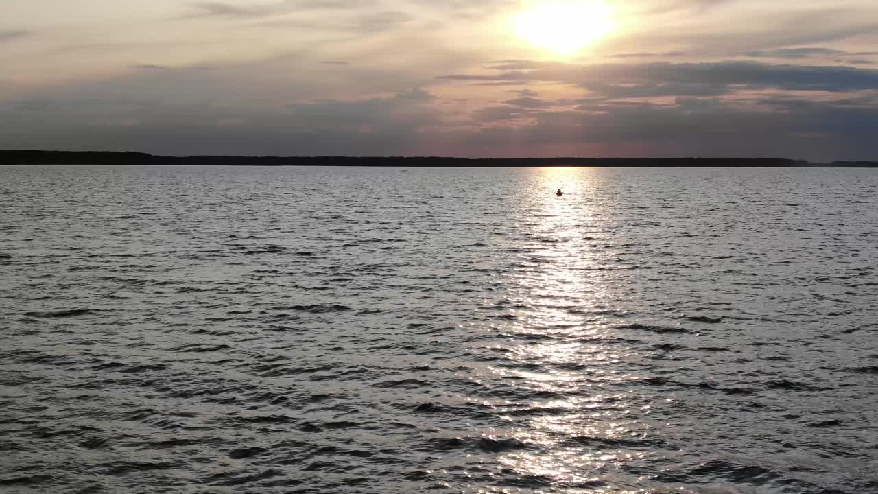 Veduta aerea bassa in volo verso una canoa in silhouette sul fiume al tramonto.