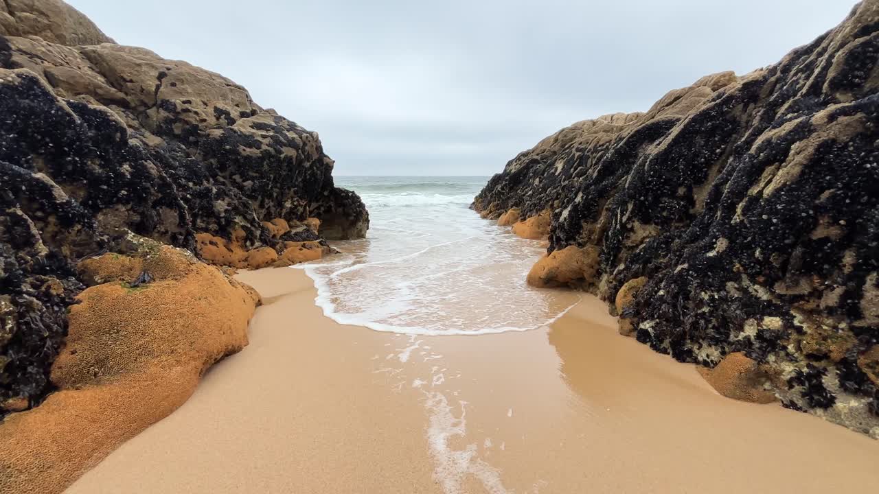 Serene Coastal Scene: Sandy Beach Between Dark Rock Formations