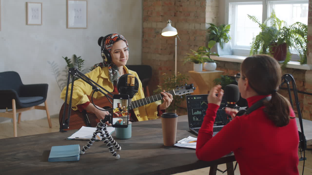 mujer cantando y tocando la guitarra durante un podcast en vivo con una presentadora