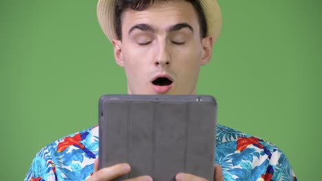 young handsome tourist man using digital tablet and looking shocked