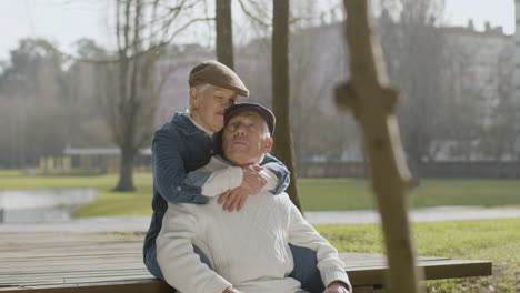 lovely senior couple looking at each other and kissing while sitting on bench in park at pond on nice autumn day 1