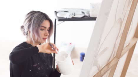 Cheerful-Latina-Girl-Holding-Gesso-White-Paint-And-A-Palette-Knife-Working-On-A-Canvas