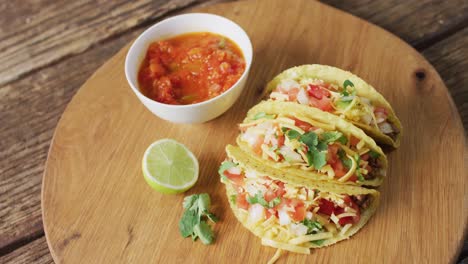 video of freshly prepared tacos and bowl with sauce lying on board on wooden surface