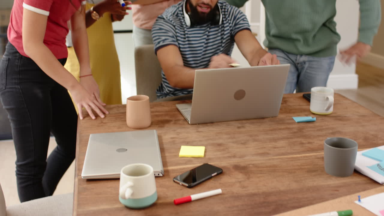 Working together, young diverse friends using laptops and smartphones at table