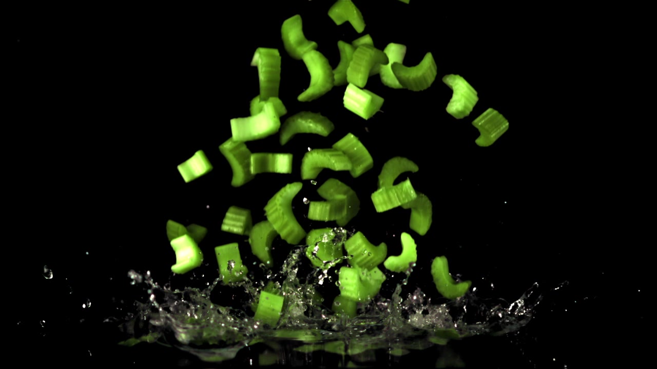 Chopped Green Celery Falling into Water with Splashes in Slow Motion