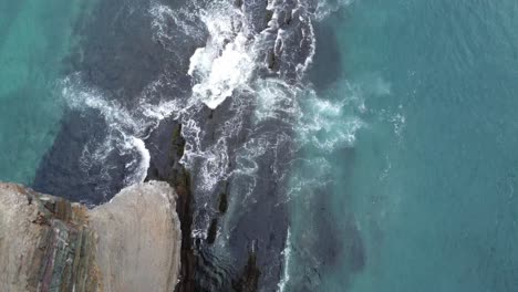 Disparo-De-Un-Dron-Sobre-El-Borde-De-Un-Acantilado-De-300-Pies-Con-Olas-Rompiendo-Contra-La-Costa-Debajo