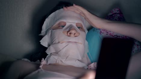 young woman in pink top with white sheet mask on face