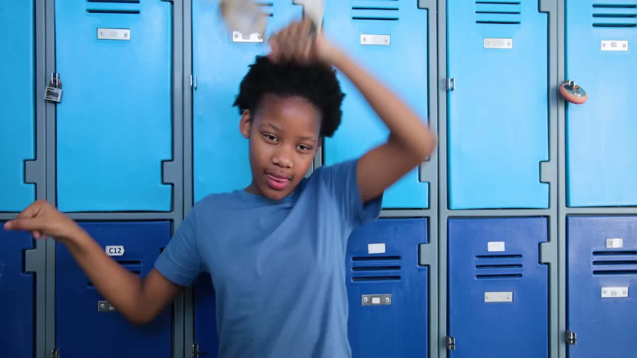 African American teen female picking up white headphones, testing fit and dancing at school lockers