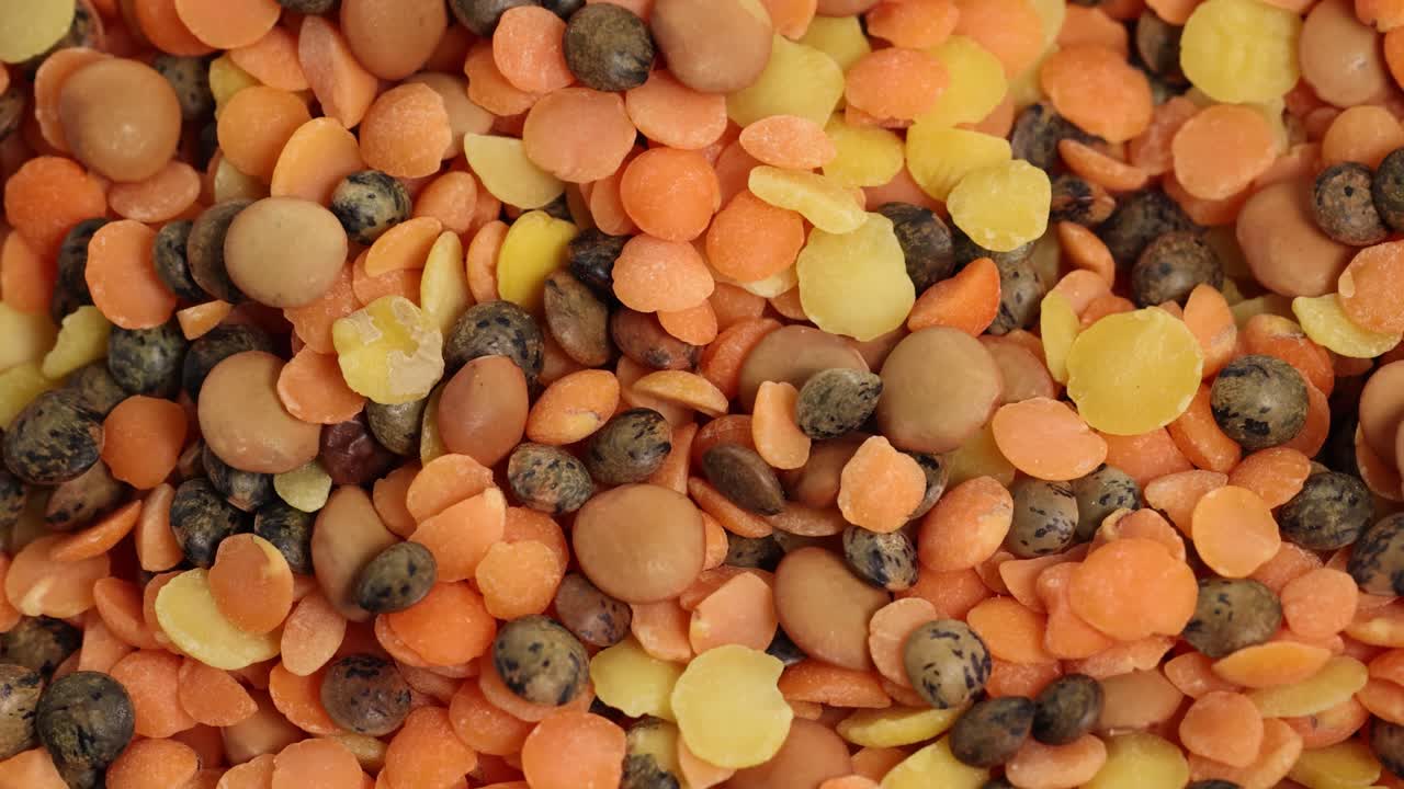 A detailed rotating view of assorted lentils and beans in warm lighting, showcasing texture and color variety