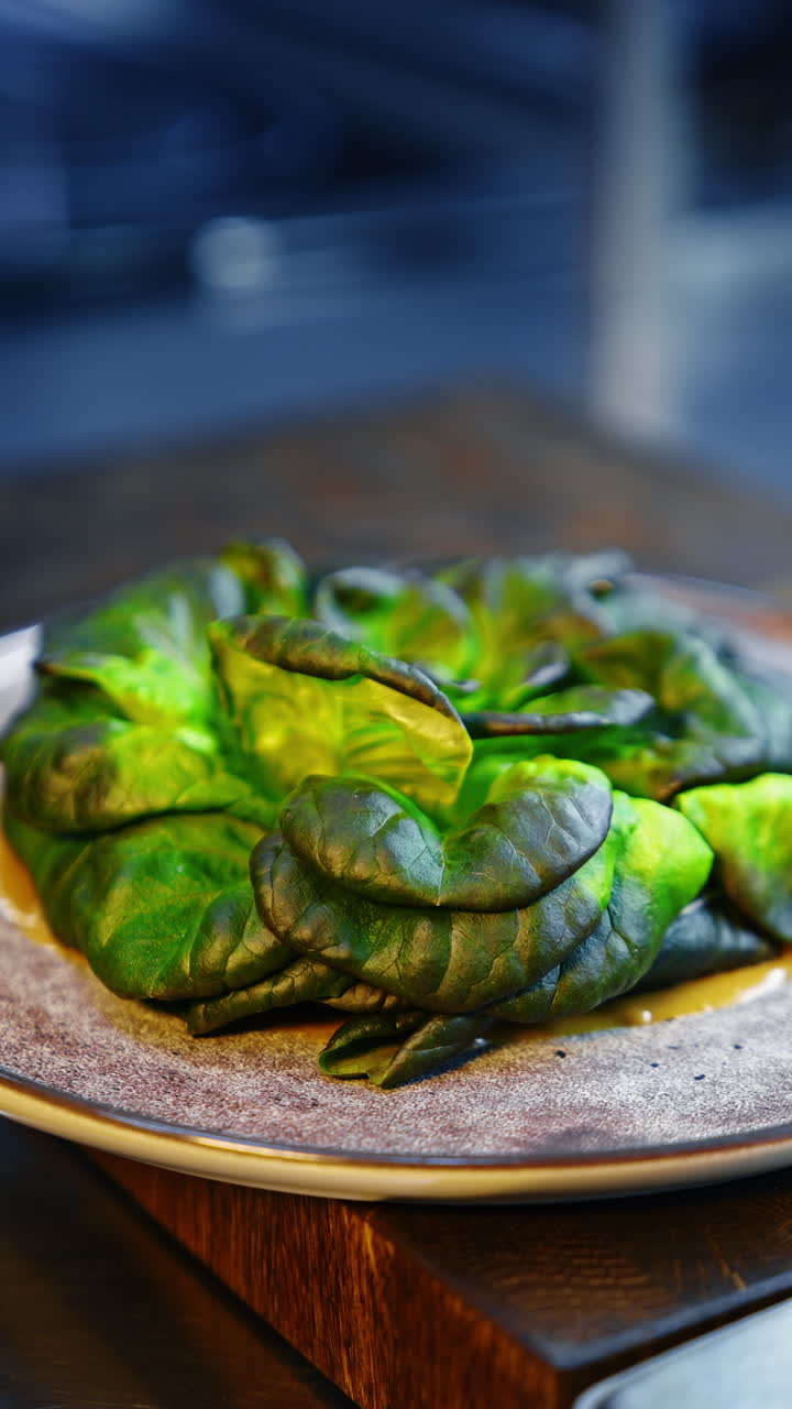 A plate with yellow sauce spread by the surface. Hands in black gloves put the green salad leaves on the dish. Close up. Vertical video.