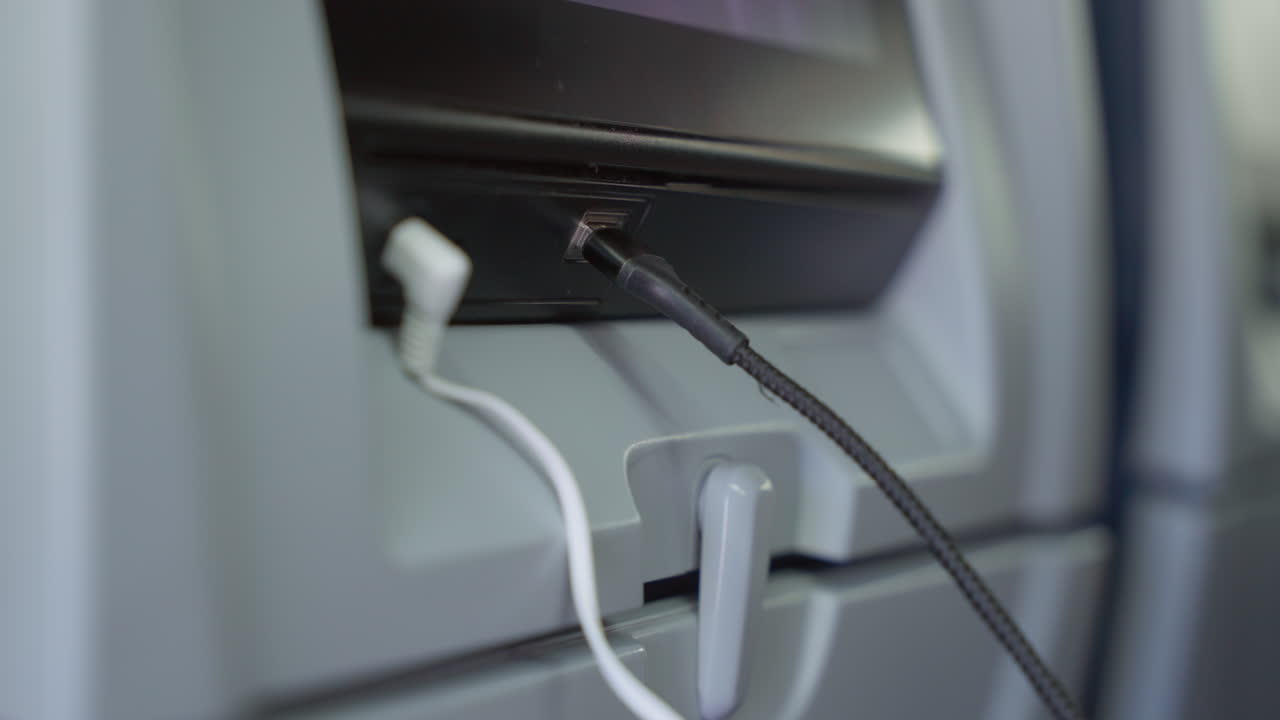 A hand plugs headphones into an entertainment screen on an airplane