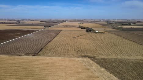 Bajo-Un-Cielo-Azul-Rural,-Campos-De-Maíz,-Medio-Oeste-De-Iowa,-Imágenes-Aéreas-De-Drones,-Marrón,-Seco,-Tierras-De-Cultivo-Y-Molinos-De-Viento-Sostenibles