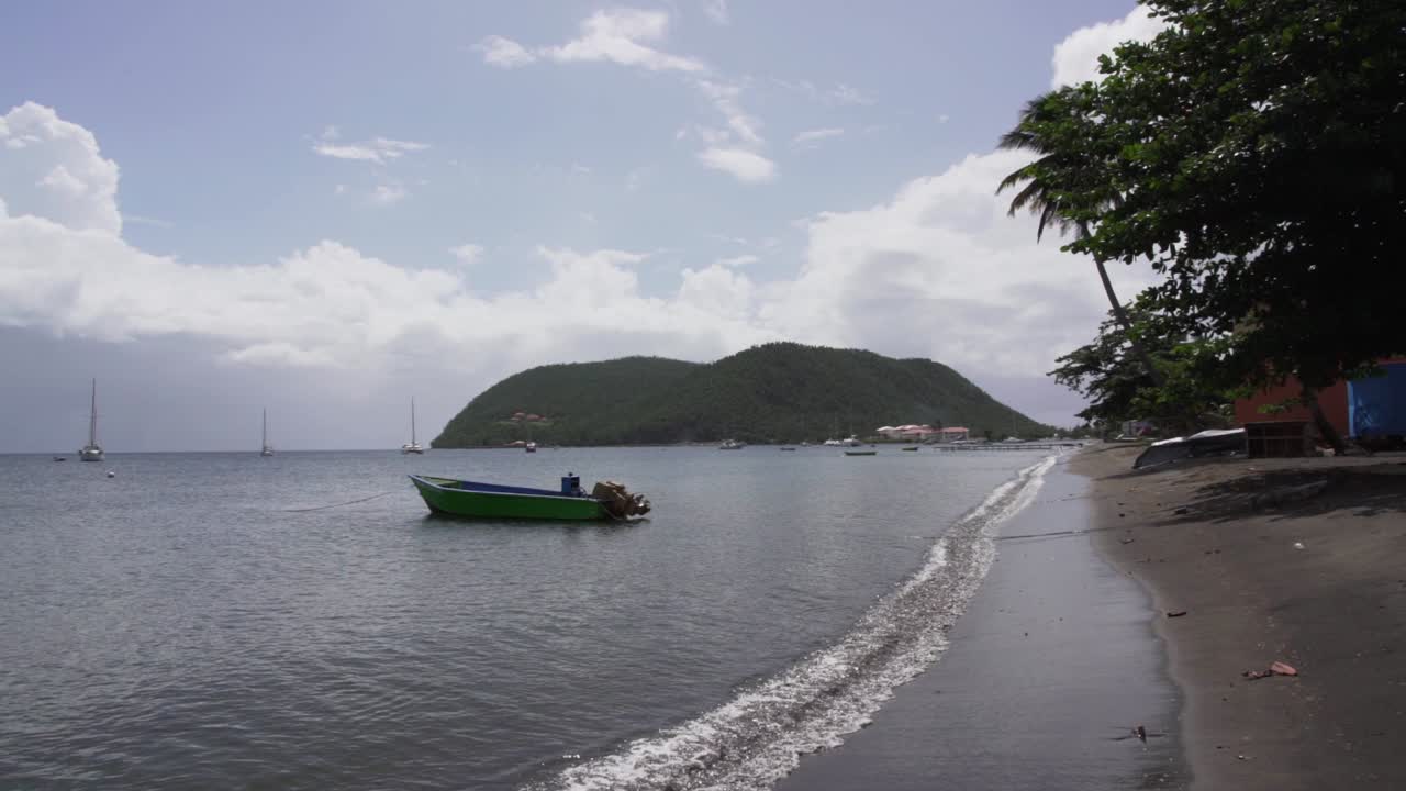 Slowmotion Pan towards the Dominica sea, beach and boat with green hill in the back