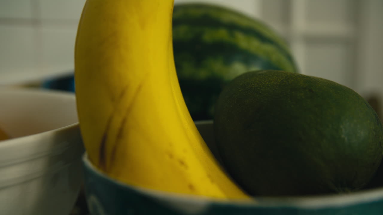 Extreme close-up of banana and mango in a ceramic fruit bowl. Natural light and shallow focus on fresh tropical fruits