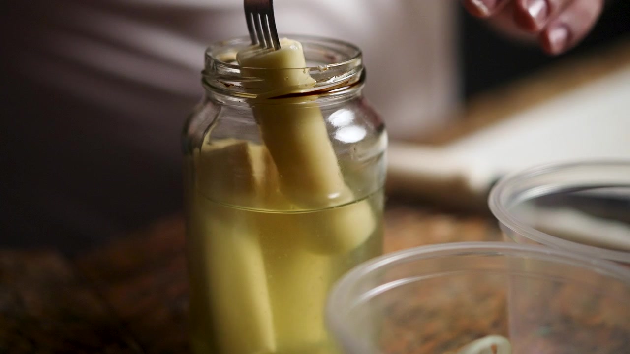 Uno chef esperto usa con cura una forchetta per sollevare un tenero cuore di palma da un barattolo di vetro, mostrando l'arte della cucina gourmet