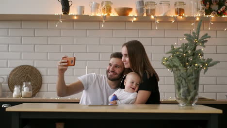 family,-parenthood-and-people-concept---happy-mother-and-father-with-baby-taking-selfie-at-home