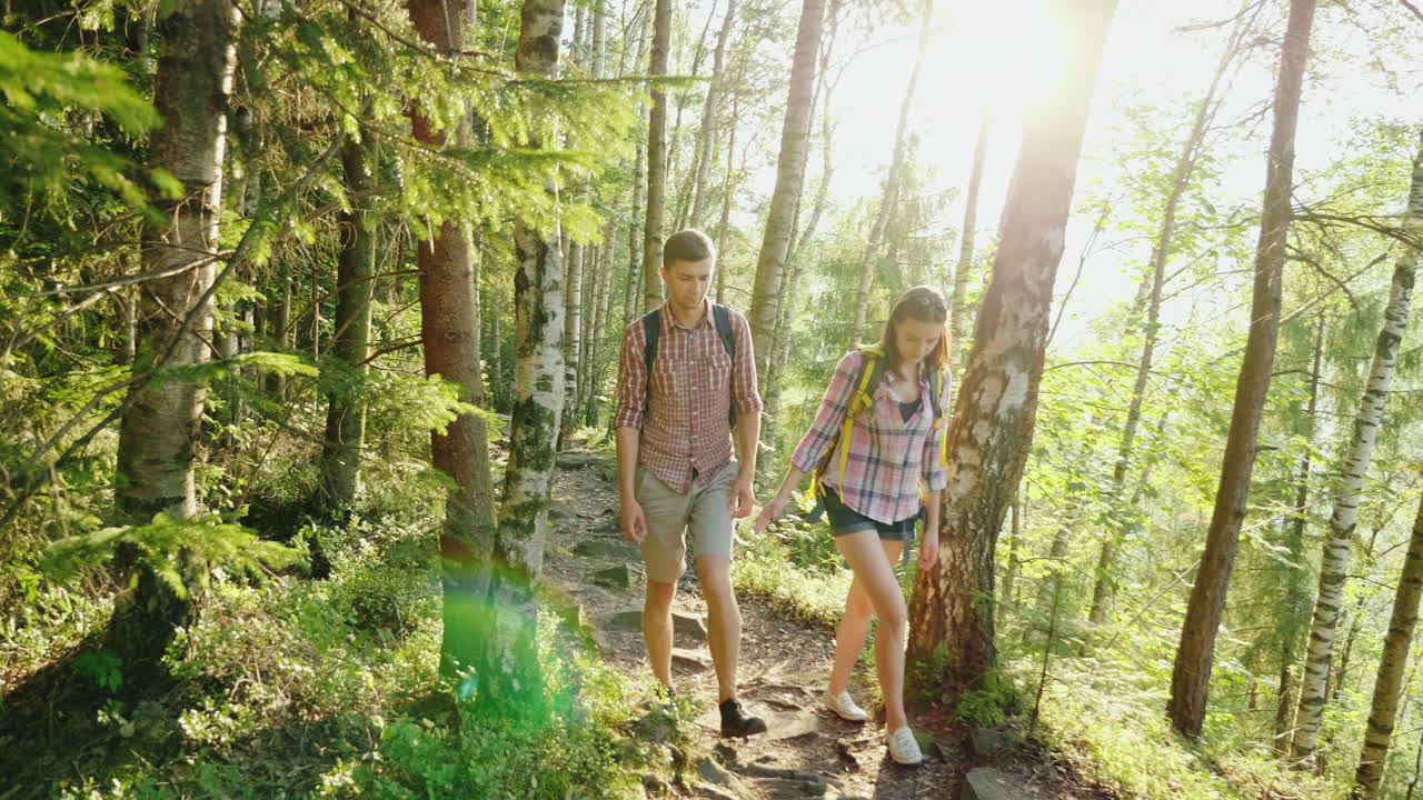 un par de turistas con mochilas van por un pintoresco sendero de montaña bajo los rayos del sol poniente