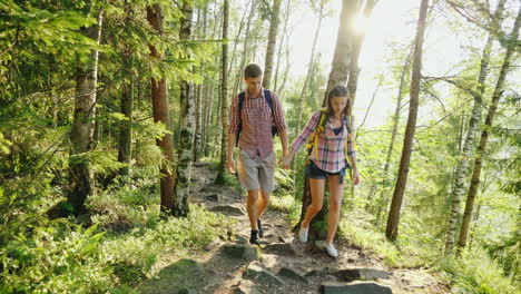 a couple of tourists with backpacks go on a picturesque mountain path in the rays of the setting sun