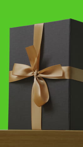 vertical video of man putting down present in gift wrapped box decorated with ribbon on table shot against green screen