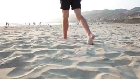 bottom half of a male with white feet and tanned legs walking along sandy beach