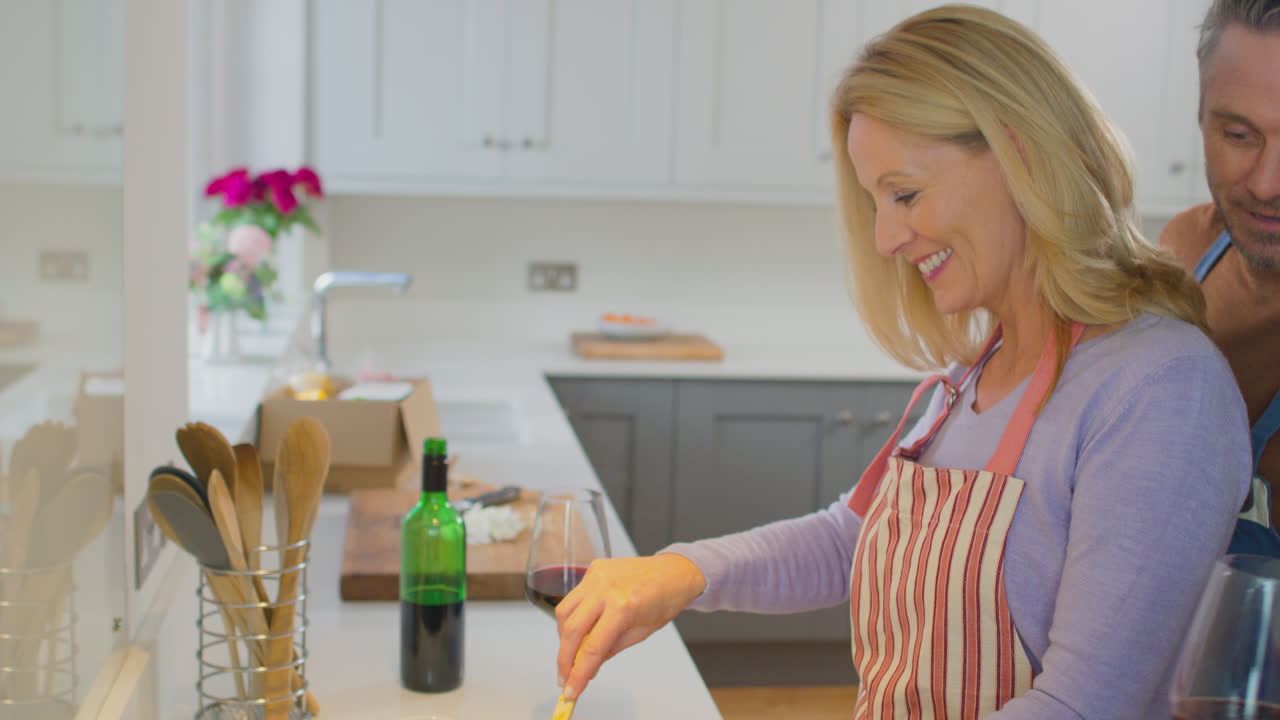Modent par med forkle drikker rødvin mens de forbereder ingredienser og lager mat hjemme sammen – filmet i sakte film