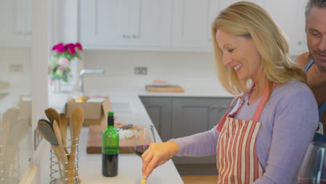 mature couple wearing aprons drinking red wine as they prepare ingredients and cook meal at home together - shot in slow motion