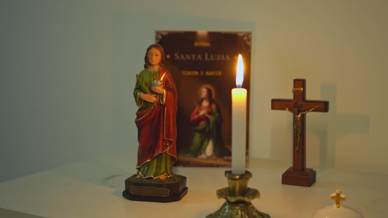 Religious setup with a statue of Saint Lucy a devotional booklet wooden crucifix and a burning candle on a table with warm light creating a sacred atmosphere for Christian prayer