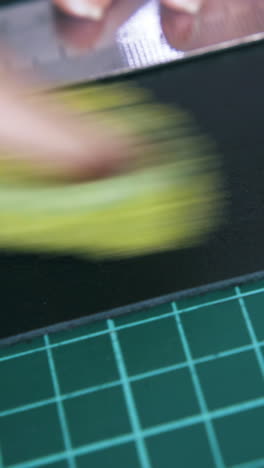 CU: Skilled tailor wipes white line on leather cloth with wet towel on green cutting board extreme close view