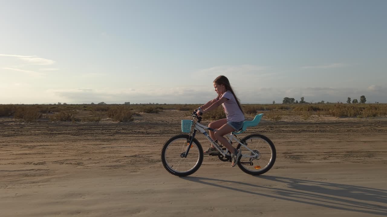 해가 어두워지면서 모래길에서 자전거를 타고 있는 어린 소녀