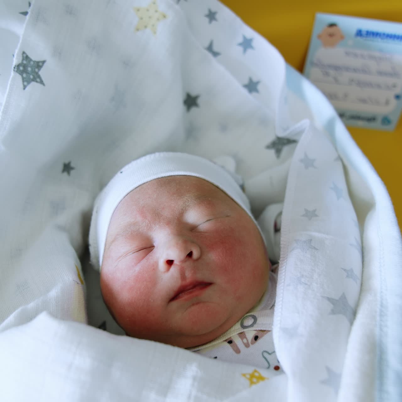 Splendido neonato caucasico con cappello e coperta. Il bambino gira la testa da un raggio di luce. Sfondo giallo