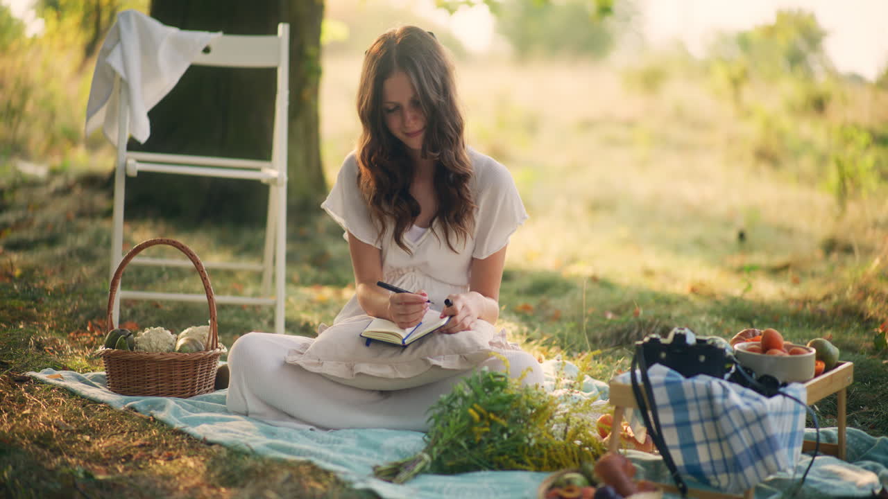 Dreamy girl writing in diary at summer picnic