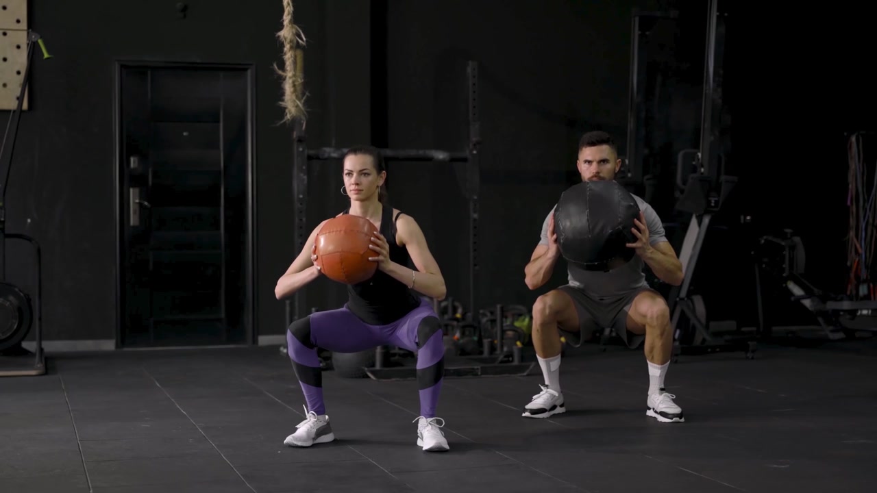 Uomo e donna che eseguono squat con palle mediche in palestra